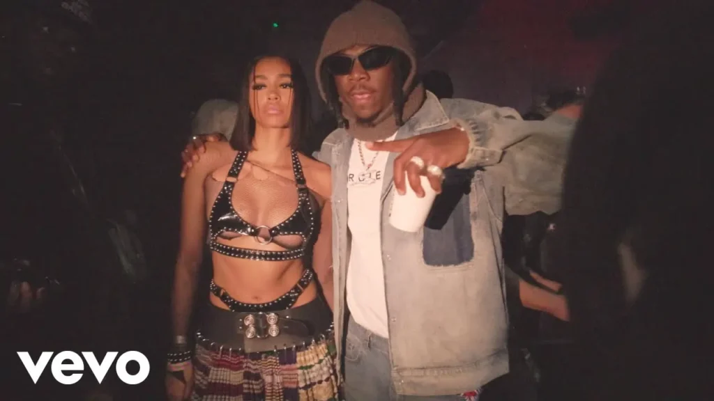 Two individuals posing together at an event, with the woman wearing a decorative top and skirt and the man in a denim jacket. thumbnail for the video "Stonebwoy, DJ Maphorisa - Apotheke (Official Video)"