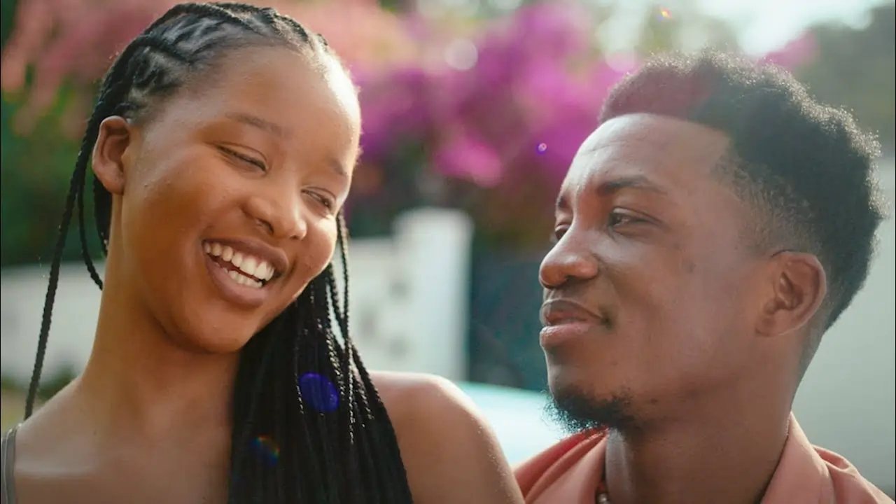 A joyful african descent couple smiling at each other, with colorful flowers in the background. Thumbanil for 'Kofi Kinaata - Effiakuma Broken Heart (Official Video)'