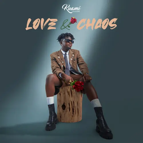 A stylish man in a brown jacket, shorts, and boots sits on a wooden stump, holding red flowers, with "love & chaos" written above in cursive. Artwork for "Kuami Eugene - Monica [INSTRUMENTAL] (ReProd By Executioner Beatz)"